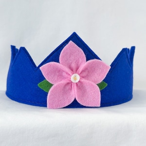 May include: A blue felt crown with a pink felt flower and green felt leaves. The flower has a white felt center.