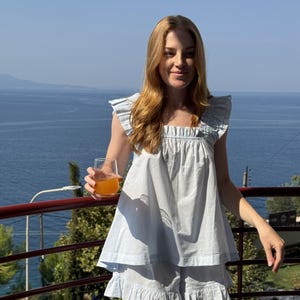 May include: A light blue two-piece set consisting of a sleeveless top and matching shorts. The top features a square neckline and ruffled shoulder details. The shorts have a ruffled hemline. The fabric is a solid light blue cotton material.