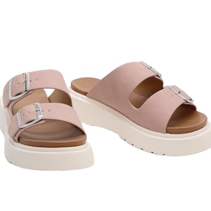 May include: A pair of light pink platform sandals with two adjustable buckles. The sandals have a white platform sole and a brown footbed.