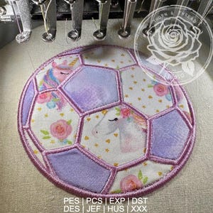 May include: Embroidered soccer ball patch featuring a unicorn design. The patch has a purple and white color scheme with floral accents. The text "THORN & THREAD STUDIO" is visible in the upper right corner. The patch is being sewn by a machine.