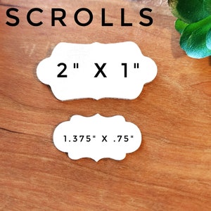 May include: Two white paper scroll tags with scalloped edges. The larger tag measures 2 inches by 1 inch. The smaller tag measures 1.375 inches by .75 inches.