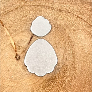 Puede incluir: Dos formas de metal plateado, una redonda y una ovalada, sobre una superficie de madera marrón claro.