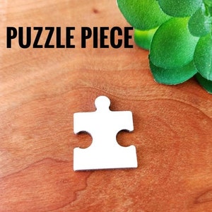 Pode incluir: Peça de quebra-cabeça de madeira branca. Mede 2,5 cm de altura e 1,9 cm de largura. "PUZZLE PIECE" está escrito em preto no topo da imagem.