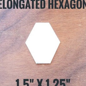 May include: White elongated hexagon shape, measuring 1.5 inches by 1.25 inches. The shape is on a wooden background.