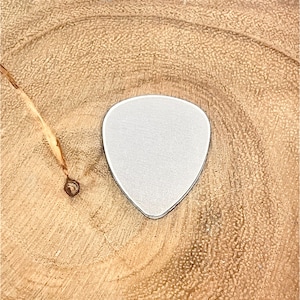 May include: A silver guitar pick on a wooden surface.