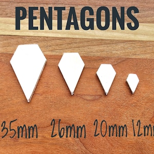 Può includere: Quattro forme di pentagoni argentati di varie dimensioni sono esposte su una superficie di legno. Il più grande è di 35 mm, seguito da 26 mm, 20 mm e il più piccolo è di 12 mm. La parola "PENTAGONS" è stampata in nero in alto.
