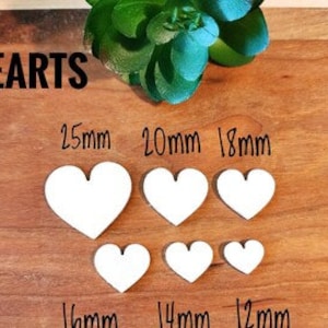 Może przedstawiać: Sześć białych drewnianych serc w różnych rozmiarach, od 12 mm do 25 mm, ułożonych w dwóch rzędach na drewnianej powierzchni.