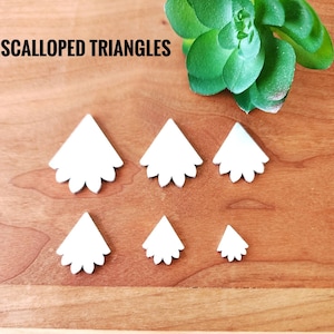 May include: Six white scalloped triangle shapes of varying sizes on a wooden surface. The text "SCALLOPED TRIANGLES" is visible at the top of the image.