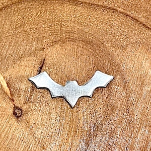 May include: A silver metal bat cutout on a brown wooden surface.