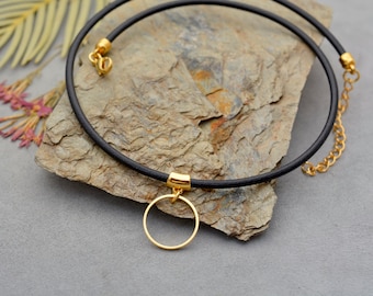 May include: A black leather choker necklace with a gold circle pendant. The necklace is adjustable and has a lobster clasp closure.