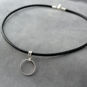 Puede incluir: Un collar gargantilla de cuero negro con un colgante circular de plata.