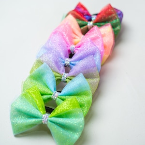 Könnte beinhalten: Ein Set aus sieben bunten Haarbändern aus glitzerndem Tüll. Die Schleifen sind in Regenbogenreihenfolge angeordnet, beginnend mit Rot und endend mit Grün.