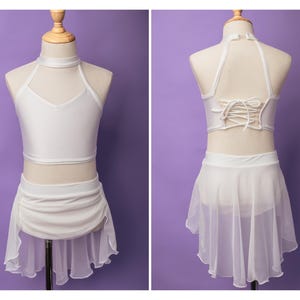 May include: A white two-piece dance outfit featuring a sleeveless crop top with a high neck and a matching skirt with a sheer, layered hem. The back of the top includes a lace-up corset-style closure with thin white fabric ties.