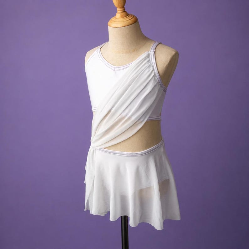 May include: A white dance leotard featuring a sleeveless bodice with a draped, semi-sheer overlay across the chest and a matching attached skirt. The garment includes thin straps and subtle silver trim along the neckline and waistline.