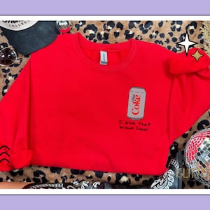 Peut inclure: Un sweat-shirt rouge vif avec un dessin de canette de Diet Coke et la phrase "I drink that brown liquor". Le motif est imprimé sur le devant du haut à col ras du cou. Le sweat-shirt est présenté sur un fond à imprimé léopard.