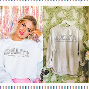 May include: A light grey crewneck sweatshirt featuring the word OPALITE in a dark, textured collegiate font across the chest, with the smaller text dancing through the lightning strikes printed directly underneath the main lettering.