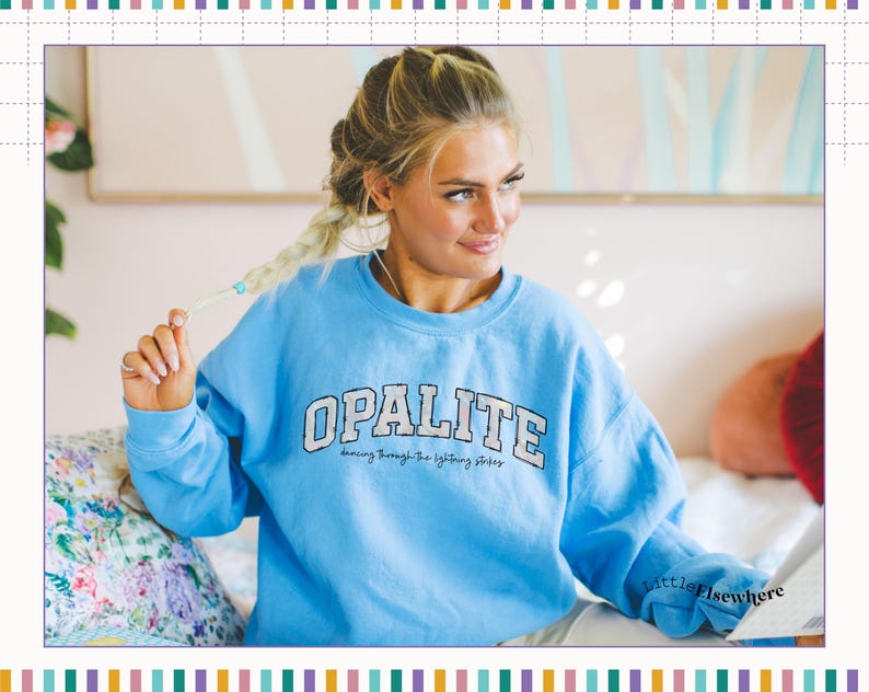 May include: A light blue crewneck sweatshirt featuring the word OPALITE in large white block letters with a dark outline, and the smaller text dancing through the lightning strikes printed underneath in a black cursive script font.