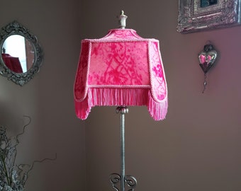 May include: A pink lampshade with a fringe trim and a floral pattern. The lampshade is on a silver lamp stand.
