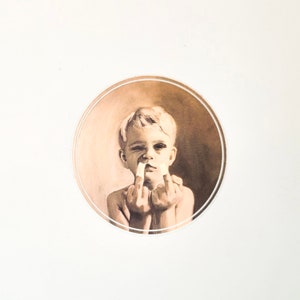 May include: A young boy with short blonde hair is shown giving the middle finger with both hands. He is wearing a white bandage on his nose.