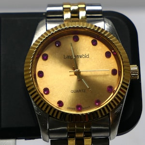 May include: A Lingenwold quartz wristwatch with a gold-toned dial featuring small red circular markers at each hour position. The watch has a fluted gold-toned bezel and a two-tone metal link bracelet in silver and gold colors. The dial displays the text Lingenwold, QUARTZ, and JAPAN MOVT.