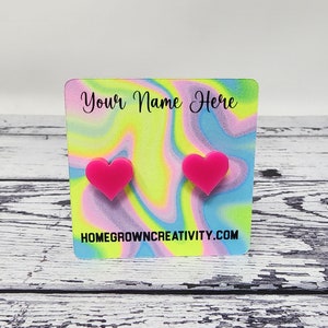 May include: A pair of pink heart-shaped stud earrings displayed on a card with the text "Your Name Here" and "homegrowncreativity.com".