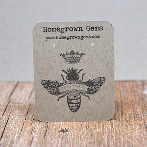 May include: A brown paper earring display card with a black and white bee illustration and the text "Be-U-tiful". The card also has a crown illustration and the text "Homegrown Gems www.homegrowngegems.com".