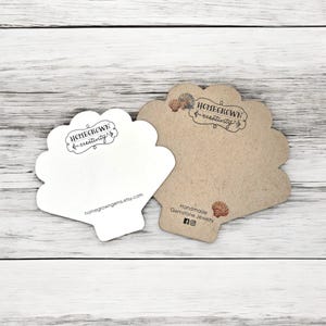 May include: Two white and brown seashell-shaped cards with the text "Homegrown & Creativity" and the website "homegrowinggems.etsy.com". The brown card also has the text "Handmade Gemstone Jewelry" and social media icons for Facebook and Instagram.