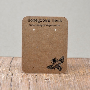 May include: Brown cardboard earring display card with the text "Homegrown Gems" and the website address "www.homegrowngegems.com". A black and white illustration of a bee with the text "Be-U-tiful" is in the bottom right corner.