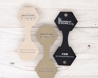 Puede incluir: Tres tarjetas de exhibición de joyería de forma hexagonal. Dos son marrones con el texto "HOMEGROWN & creativity" y "Handmade Jewelry homegrowngems.etsy.com". La tercera es negra con el texto "SONORAN CHARM Jewelry" y "www.SonoranCharm.com ♪".