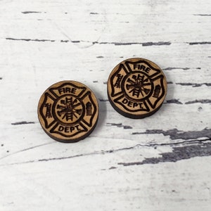 May include: Two wooden round buttons with a fire department logo. The logo is a cross with a fire hydrant, an axe, and a ladder in the center. The words "FIRE DEPT" are written around the logo.