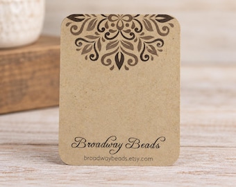 May include: A rectangular light brown kraft paper display card with rounded corners. The top features a dark brown symmetrical floral pattern. The bottom displays the text Broadway Beads in a script font and broadwaybeads.etsy.com in sans-serif.