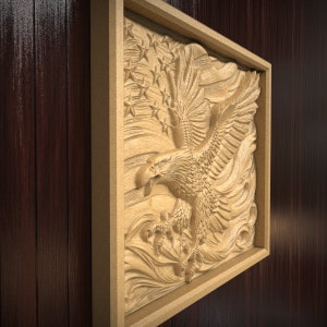 May include: A wooden carving of an eagle with its wings spread wide, flying over a stylized American flag. The carving is mounted in a wooden frame.