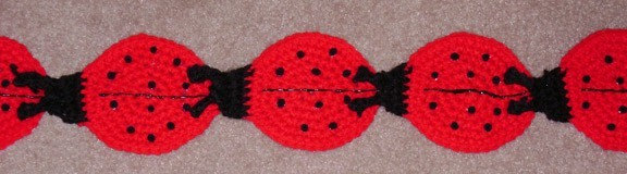 May include: A row of five crocheted ladybug ornaments with black wings and red bodies with black dots.