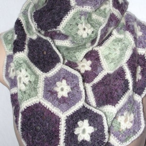 May include: A crocheted scarf with a hexagonal pattern in shades of purple, green, and white. The scarf features a repeating flower design.