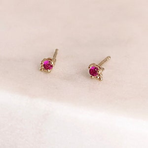 May include: A pair of gold stud earrings with a small pink gemstone in the centre of each earring.