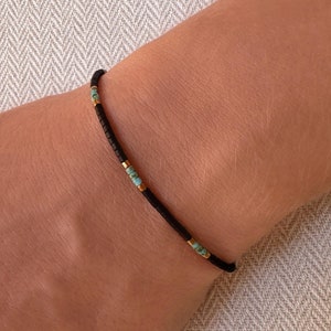 Könnte beinhalten: Ein schlichtes Armband aus schwarzen Perlen mit kleinen türkisfarbenen und goldenen Perlen.
