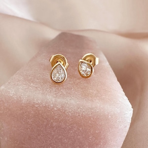 Könnte beinhalten: Ein Paar goldene Tropfenohrringe mit klaren birnenförmigen Edelsteinen.