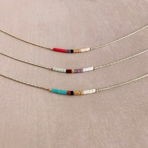 Peut inclure: Trois colliers en chaîne dorée avec des perles de différentes couleurs. Le collier du haut a des perles roses, noires et blanches. Le collier du milieu a des perles bleu clair, marron et violettes. Le collier du bas a des perles turquoise, noires, dorées et blanches.