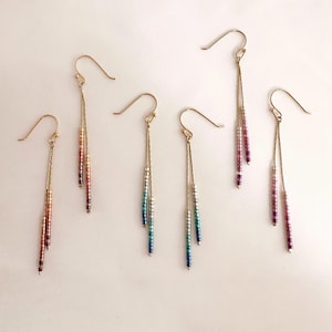 Può includere: Sei paia di orecchini pendenti con ganci e catene color oro. Gli orecchini presentano fili di perline verticali in varie sfumature di colore, tra cui rosso, arancione, viola, blu e verde. Le perline sono piccole e creano un look elegante.