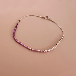 Peut inclure: Bracelet délicat avec un dégradé de petites perles carrées dans des tons roses et violets. Les perles passent du violet foncé au rose clair, enfilées sur une fine chaîne dorée. Fermeture par fermoir mousqueton.