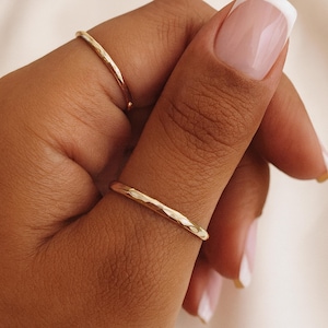 Könnte beinhalten: Nahaufnahme von zwei goldfarbenen, gehämmerten Ringen. Die Ringe sind dünn und haben eine strukturierte Oberfläche. Die Ringe werden an Fingern getragen, wobei ein Ring am Zeigefinger und der andere am Mittelfinger ist. Die Nägel sind mit French Manicure lackiert.