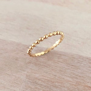 May include: A delicate gold ring with a beaded design. The ring is made of a thin band of metal with small, round beads evenly spaced along the band.
