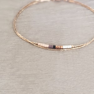 May include: A delicate gold chain bracelet with a small row of colorful beads in shades of beige, brown, black, and white.