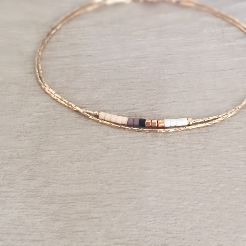 May include: A delicate gold chain bracelet with a small row of colorful beads in shades of beige, brown, black, and white.
