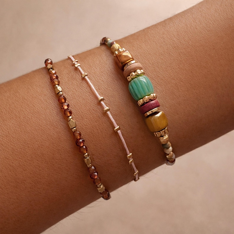 May include: Three beaded bracelets in shades of brown, gold, and pink. One bracelet features small, round brown beads and gold-coloured square beads. Another is a delicate pink string with gold accents. The third bracelet has a mix of colourful beads.