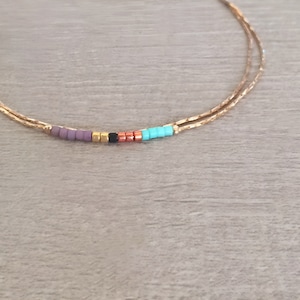 May include: A gold chain bracelet with a row of colorful beads. The beads are purple, gold, black, copper, and turquoise.