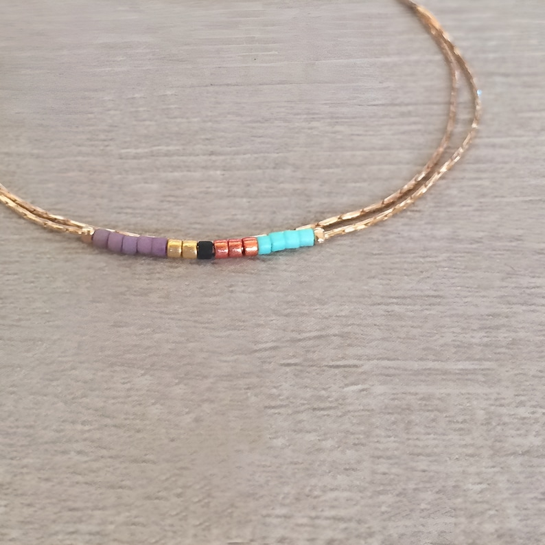 May include: A gold chain bracelet with a row of colorful beads. The beads are purple, gold, black, copper, and turquoise.