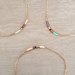 May include: Three gold chain necklaces with colorful beads. Each necklace has a different color scheme, including pink, purple, turquoise, and black beads.