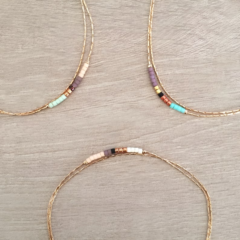 May include: Three gold chain necklaces with colorful beads. Each necklace has a different color scheme, including pink, purple, turquoise, and black beads.