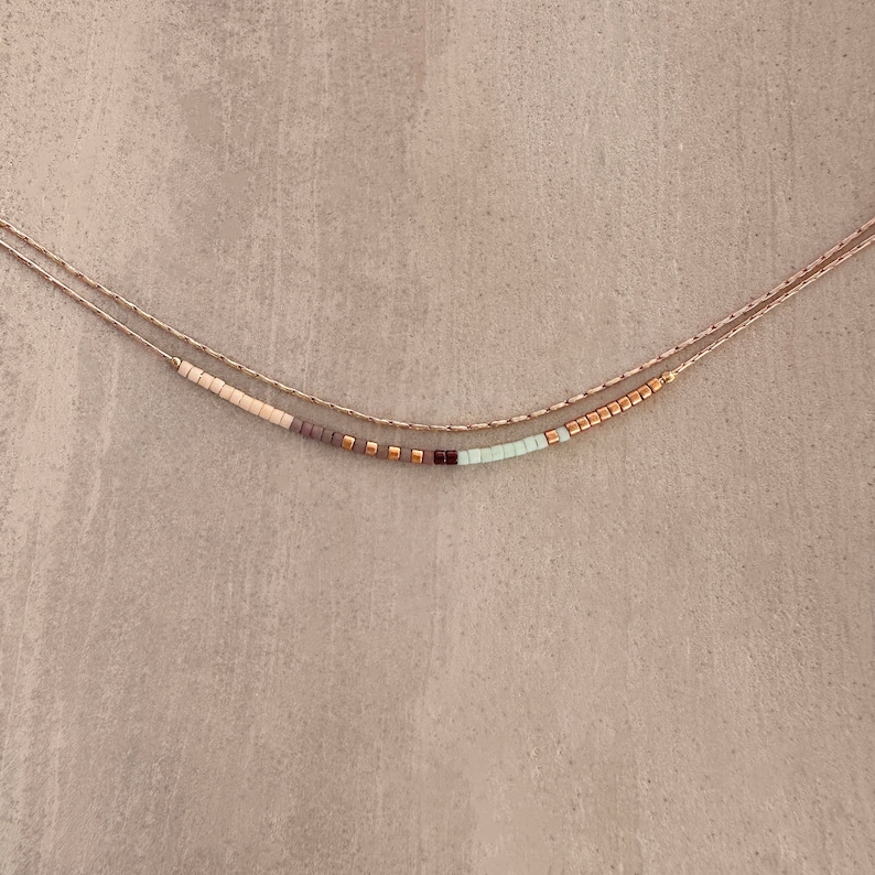 May include: A delicate gold chain necklace with a row of small, colorful beads. The beads are in shades of beige, brown, purple, and light green.